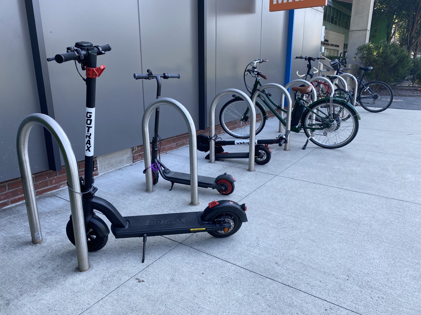 Two scooters followed by several bicycles parking in a row outside.