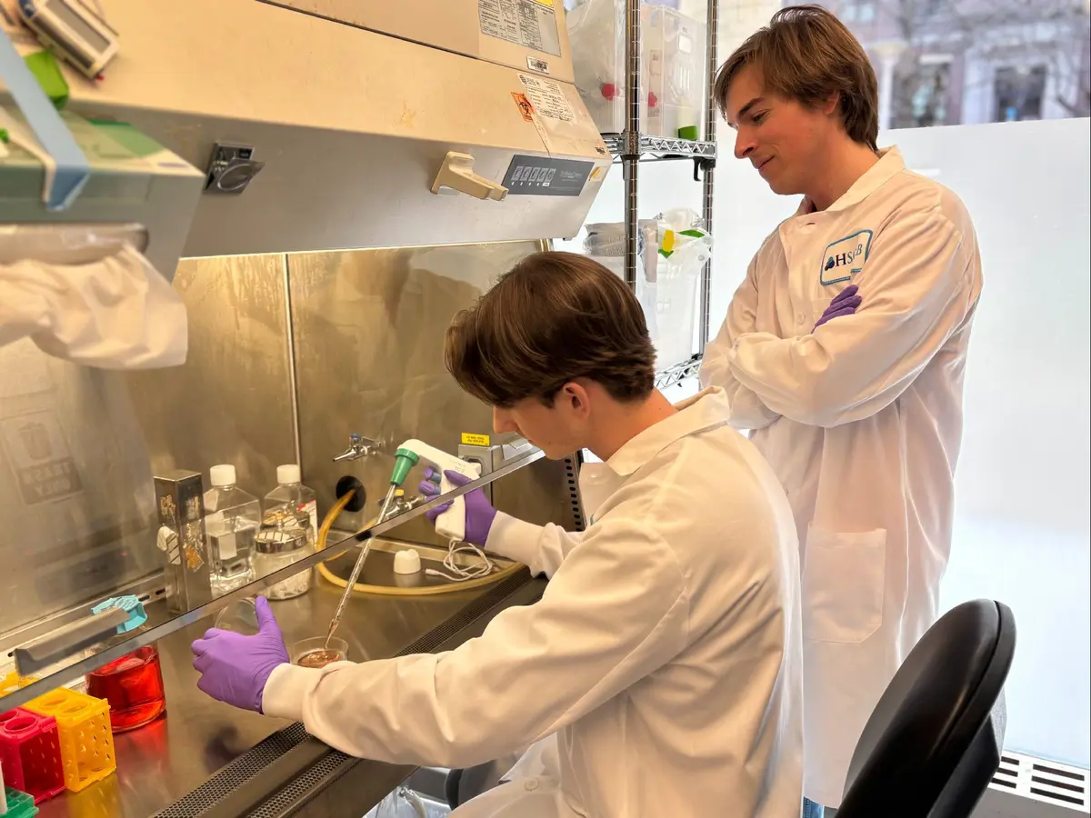 Two researchers in white lab coats, one seated, the other standing in lab