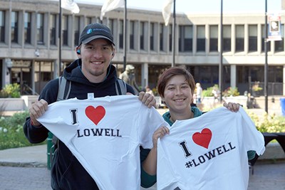 Two students pose for a photo while holding up shirts that say I love Lowell