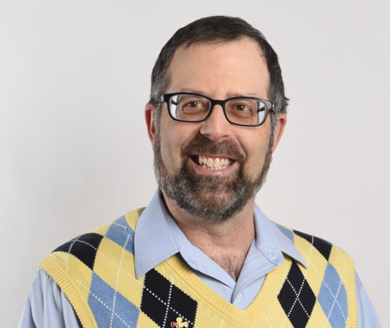 Stephen Shore wearing glasses and a plaid sweater vest over a blue collared shirt smiling at the camera.