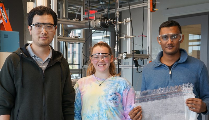 Sid Iyer stands in the lab with two other students holding a piece of smart fabric