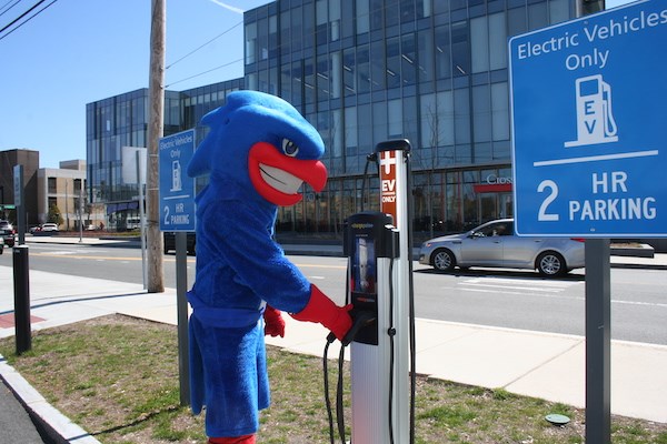 Rowdy the River Hawk using an electrical vehicle charging station on campus