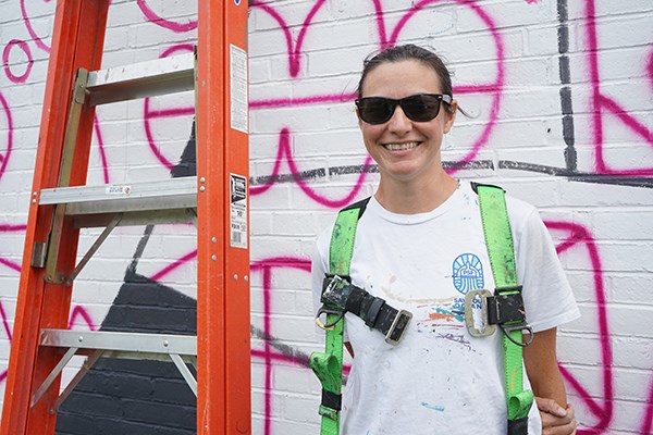 New England mural artist Sophy Tuttle in front of the graffiti grid for her mural on UMass Lowell's South Campus