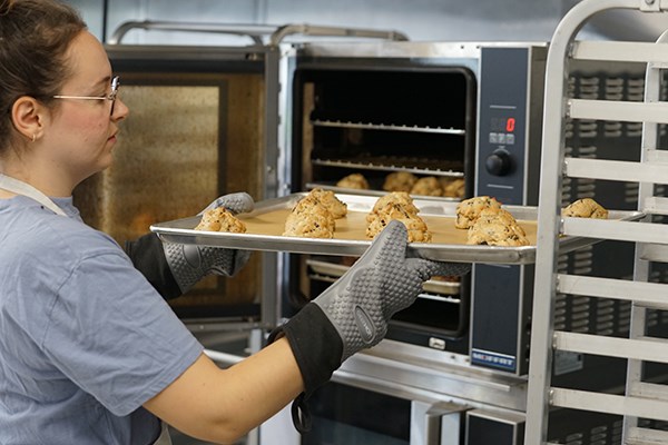 A young woman pulls a tray of freshly baked cookies from an oven