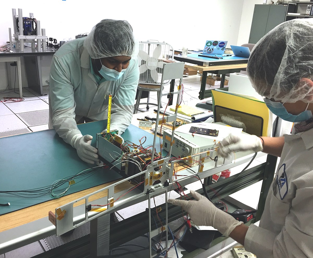 Two students in a lab working on a equipment that is part of a satellite