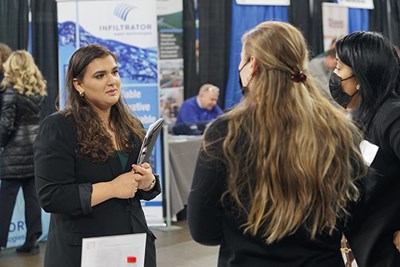 A woman holding a folder talks to two women at a career fair