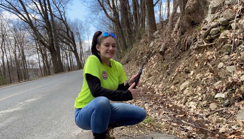 Stefany Campbell at the edge of a road holding a device to measure water samples
