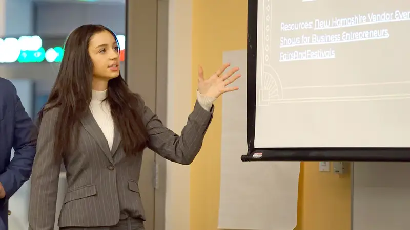 UMass Lowell business student Stephanie Carpenito presents in front of a screen.