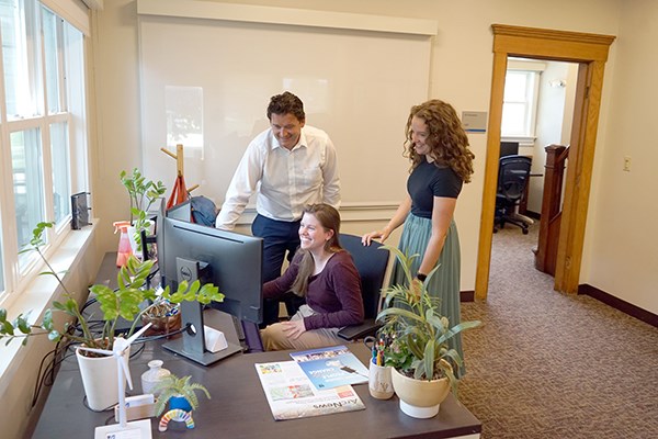 A man and two women look at a computer monitor in an office