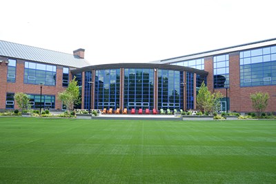 An exterior photo of a brick building with tall windows and green turf in front