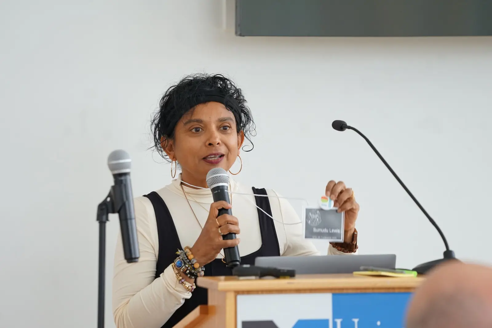 Clinical Professor of Education Sumudu Lewis stands holding a mike in front of a podium