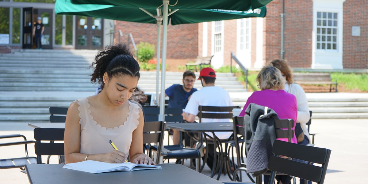 Sunilda Frias writes in a notebook at a table outside the library on North Campus