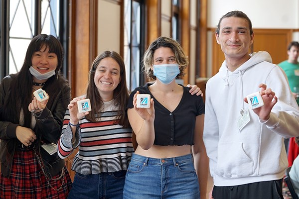 Three young women and a young man pose for a photo while holding cookies with the UMass Lowell logo on them