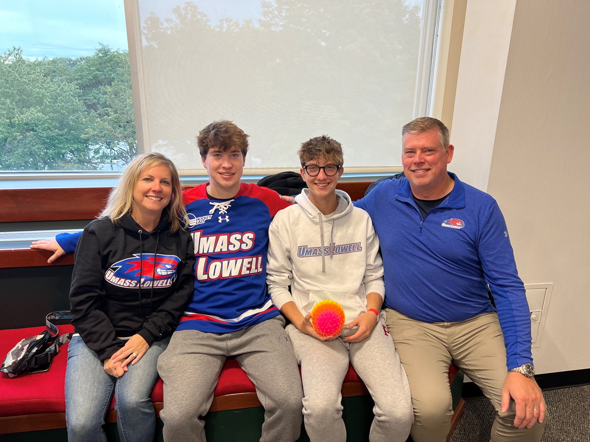 Mother, 2 sons and a Father all dressed in UMass Lowell gear pose for a photo.