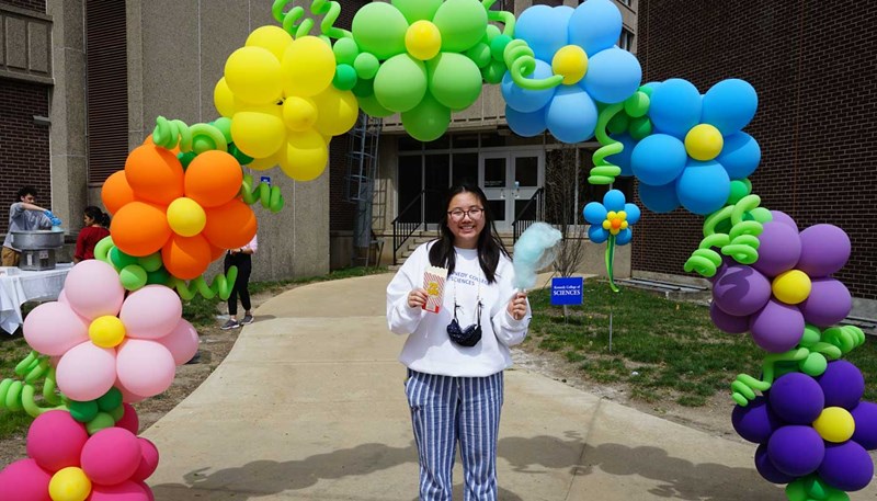Tanya Kieu holds cotton candy and popcorn below an arch of balloon flowers at UMass Lowell's SpringFest.