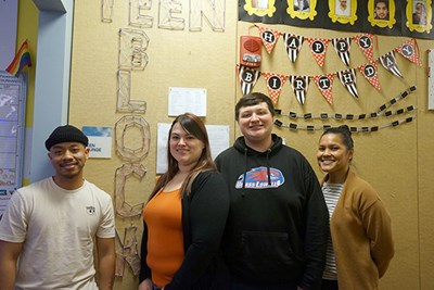 Four people pose for a photo while standing in front of a wall with the words "Teen BLOCK" 