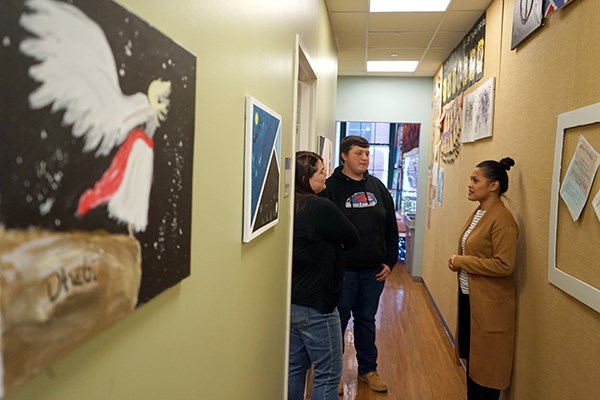 Three people chat in a hallway that is lined with student artwork