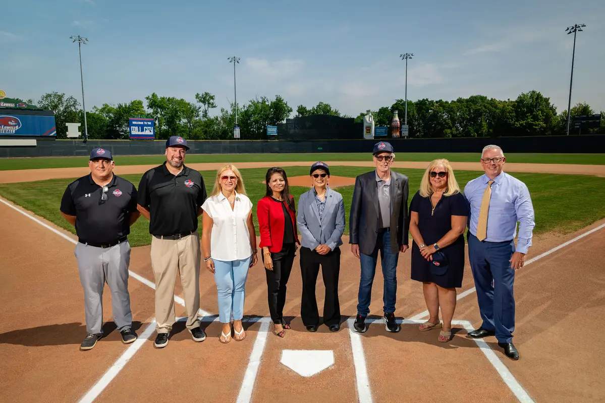 Eight men and women standing at home plate on baseball field