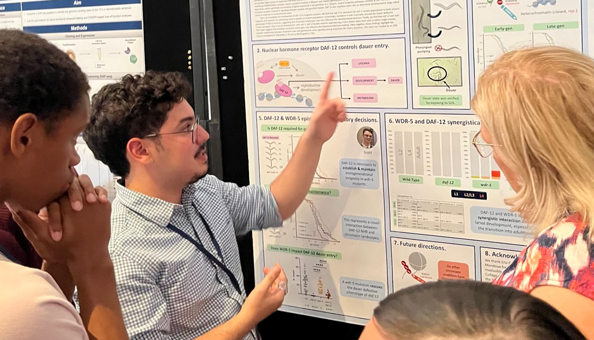 Thiago Borges points to a research poster as others look on.