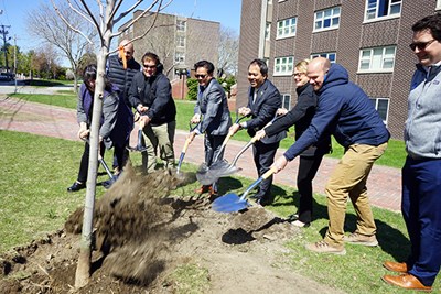 A group of people shovel dirt onto a planted tree as part of a ceremony
