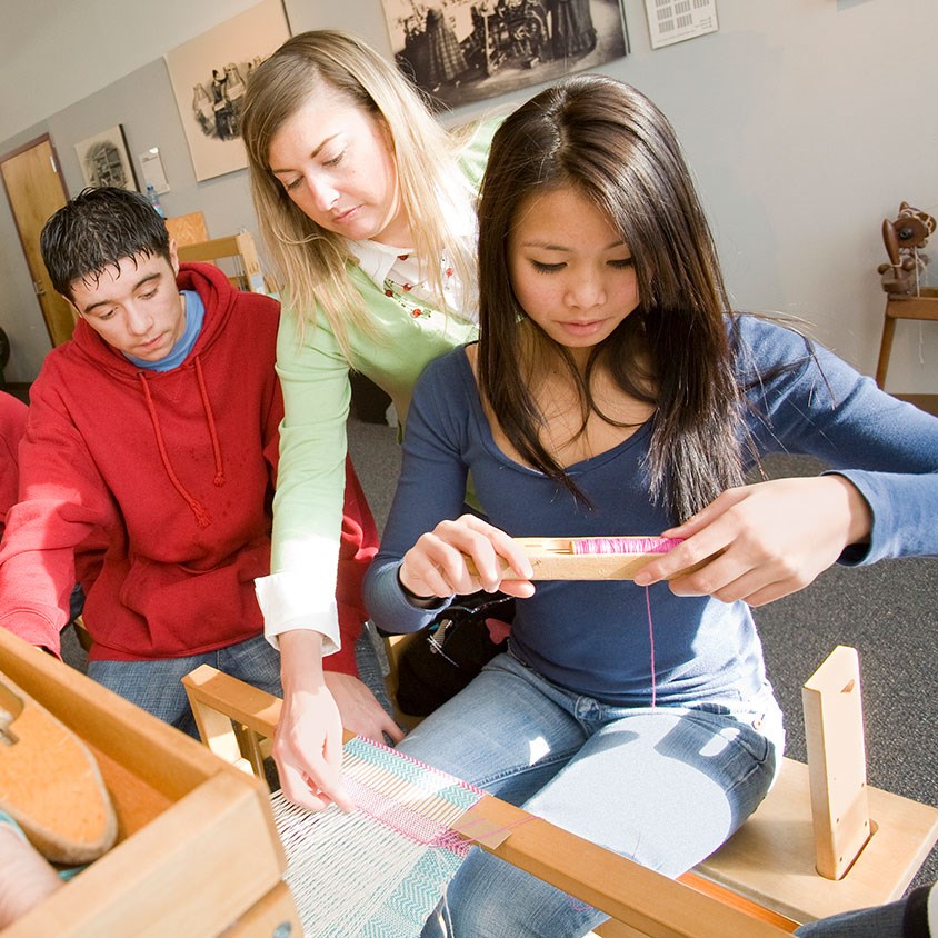 Teenagers and instructor at a loom learning how to weave at the Tsongas Industrial History Center