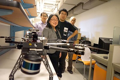 Professors and a postdoctoral researcher stand behind a drone.