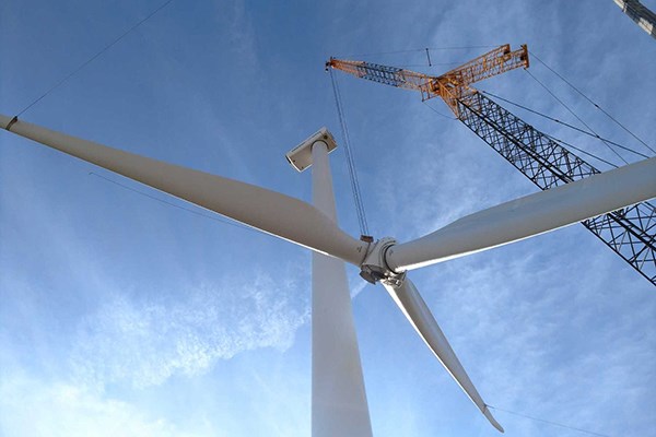 A construction crane lifts wind turbine blades onto a base