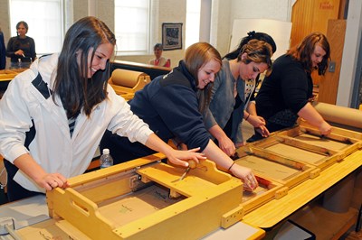 Smiling students use museum equipment to practice mass printing techniques