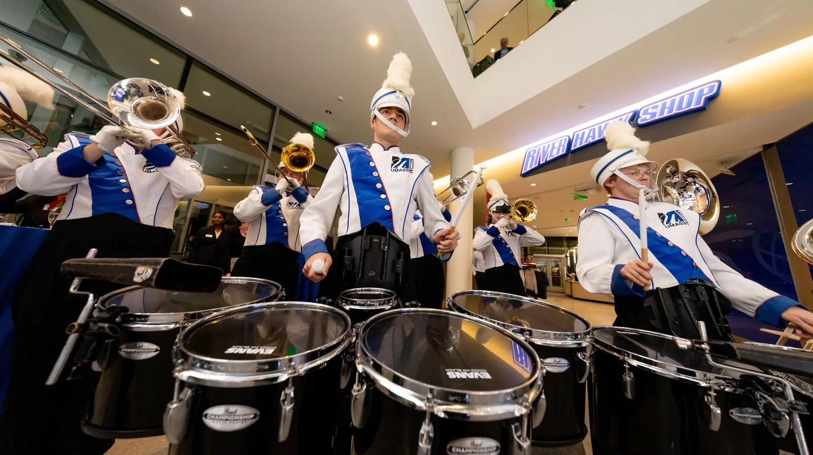 UMass Lowell student drummer and horn players march inside University Crossing