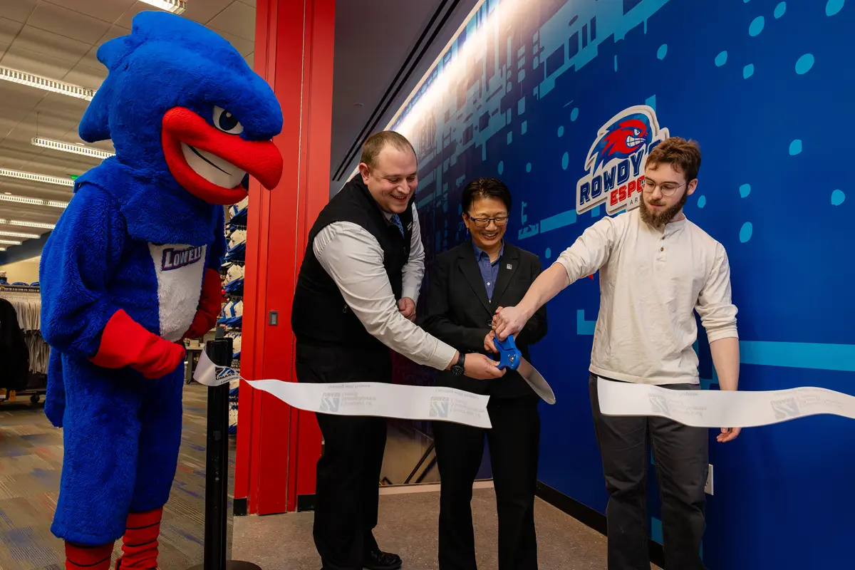 Three people cut a ceremonial ribbon while a red, white and blue bird mascot looks on.