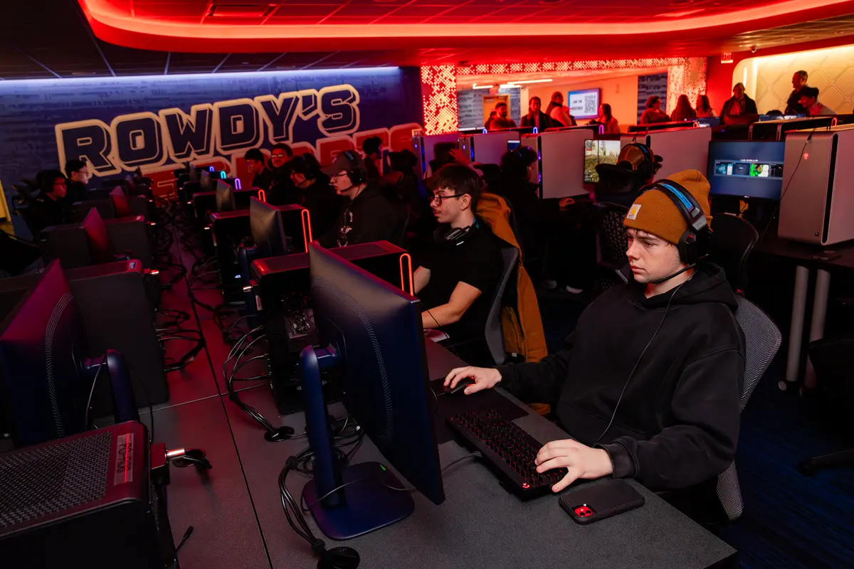 Three people cut a ceremonial ribbon while a red, white and blue bird mascot looks on.