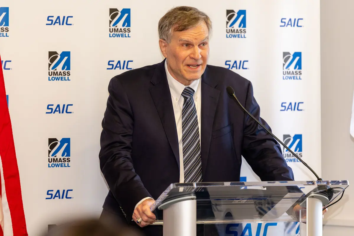 Vinnie DiFronzo of SAIC stands at a podium in front of a banner with UMass Lowell and SAIC logos 