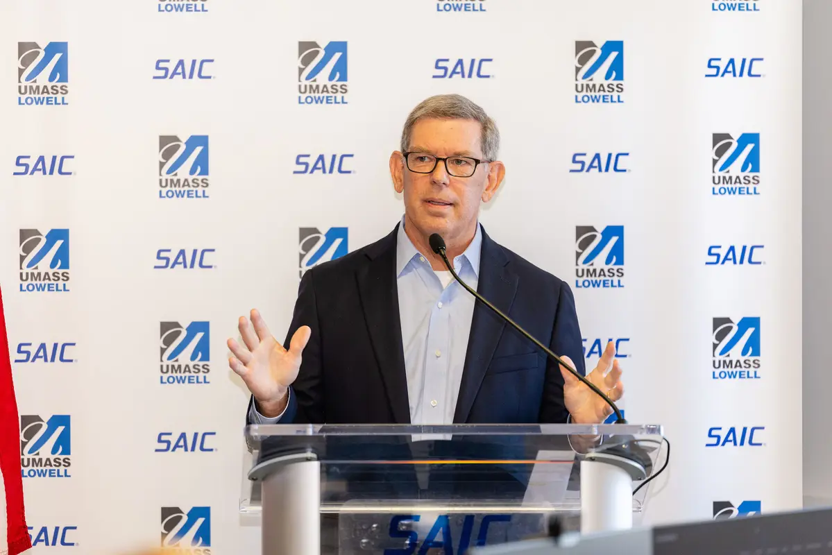 Cybertrust Massachusetts CEO Peter Sherlock speaks from a podium in front of a banner with UMass Lowell and SAIC logos