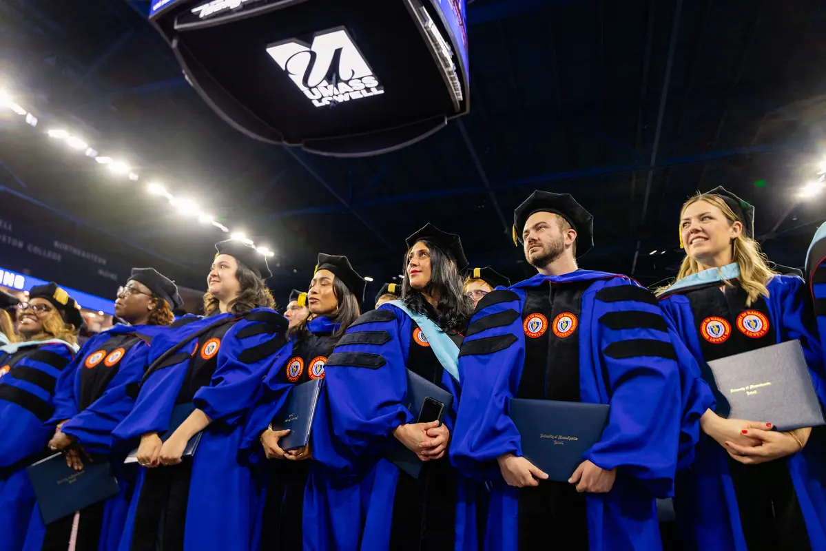 UMass Lowell doctoral graduates in their blue robes stand during commencement