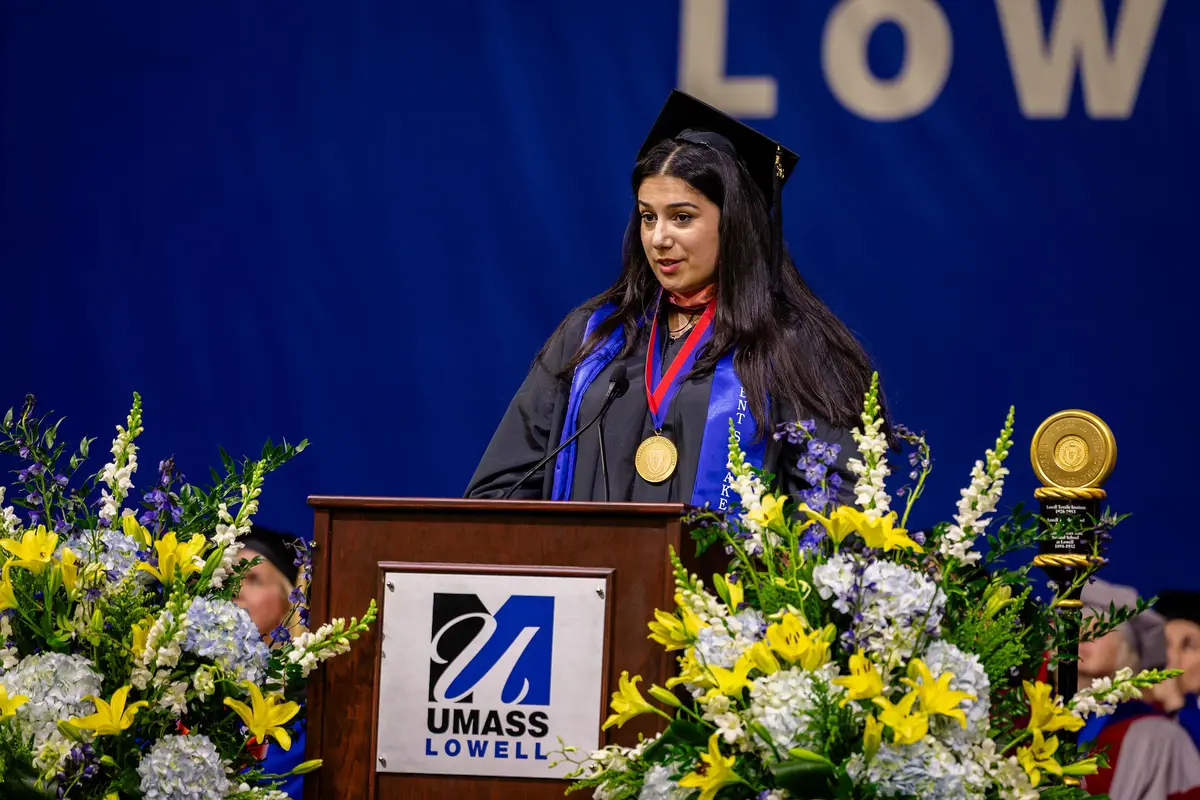 Student commencement speaker Yasi Nejad gives a speech from a podium labeled with the UMass Lowell logo