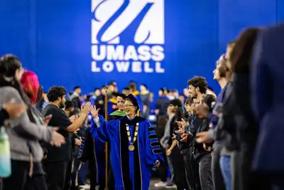UMass Lowell doctoral graduates in their blue robes stand during commencement