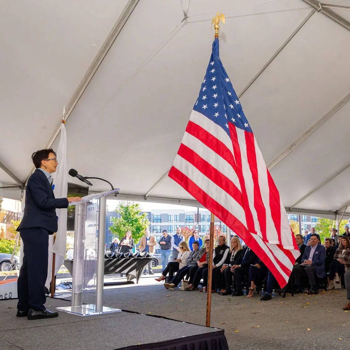 UMass Lowell Chancellor, Julie Chen, speaks to a large crowd at the Draper opening ceremony. A U.S. flag is in the foreground.