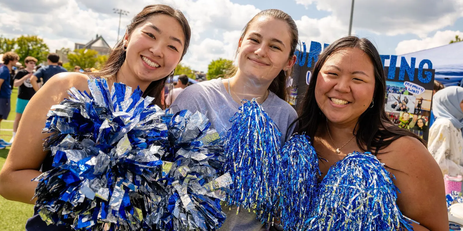 Three students, smiliing, at the Engagement Fair holding pom poms.