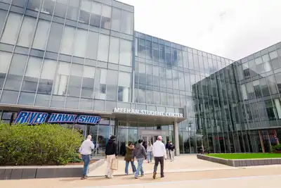 Students walk into the front of the Meehan Student Center at UMass Lowell, where the River Hawk Shop is located