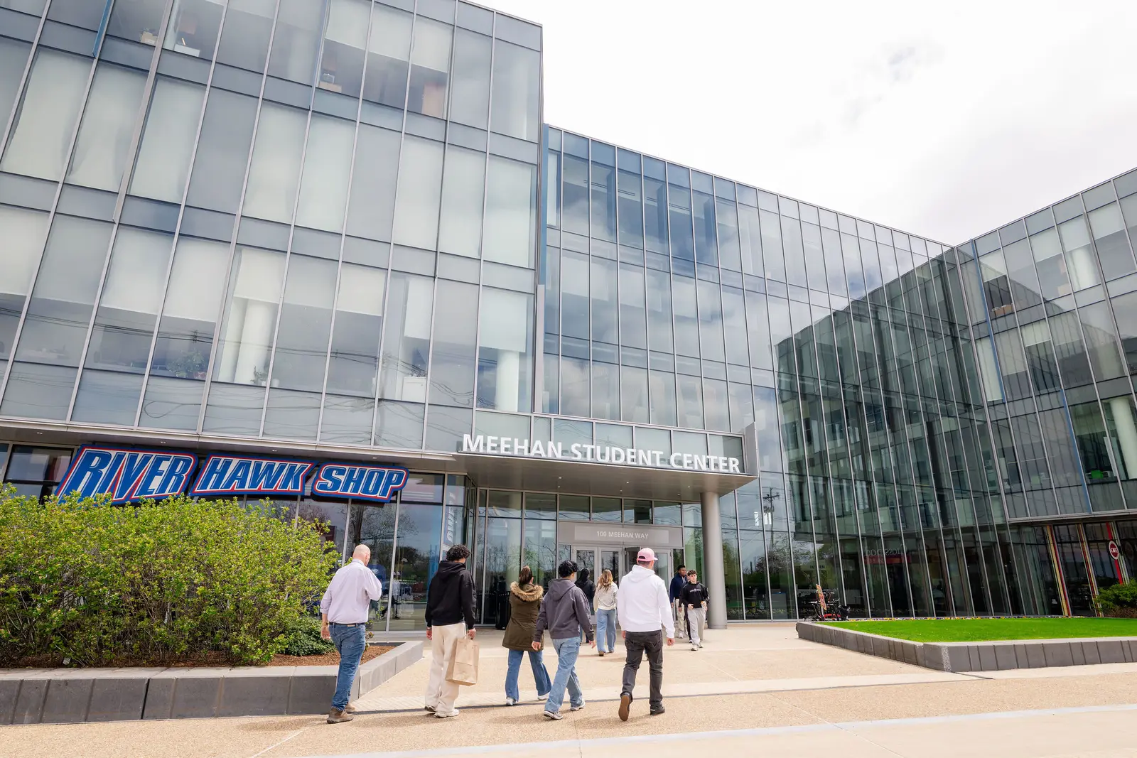 Students walk into the front of the Meehan Student Center at UMass Lowell, where the River Hawk Shop is located