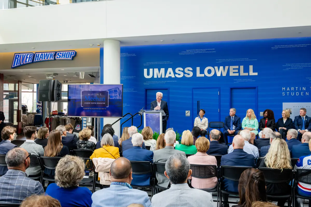 UMass President Marty Meehan stands at a podium on a stage in front of an audience in the Meehan Student Center atrium