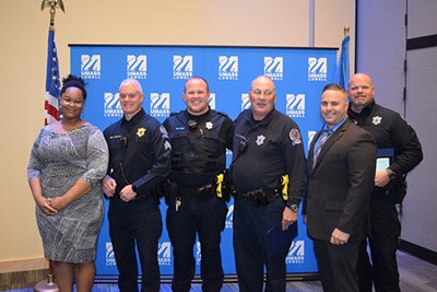 A woman wearing a dress, a man in a suit and four men in police uniforms pose for a photo