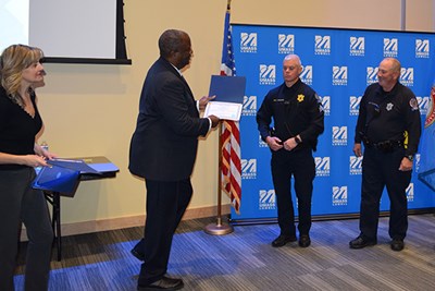 A man in a suit presents a certificate to a police officer while a woman and another officer look on