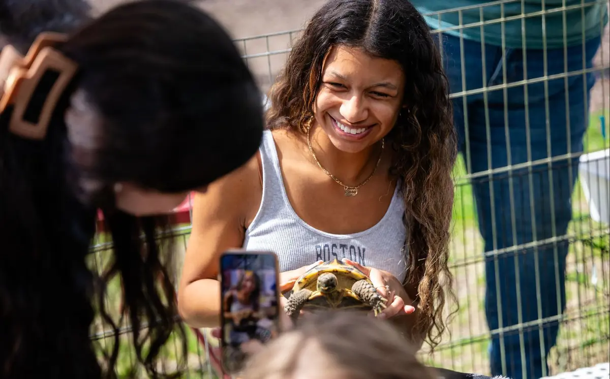 Girl smiles holding turtle while friend takes cell photo of her
