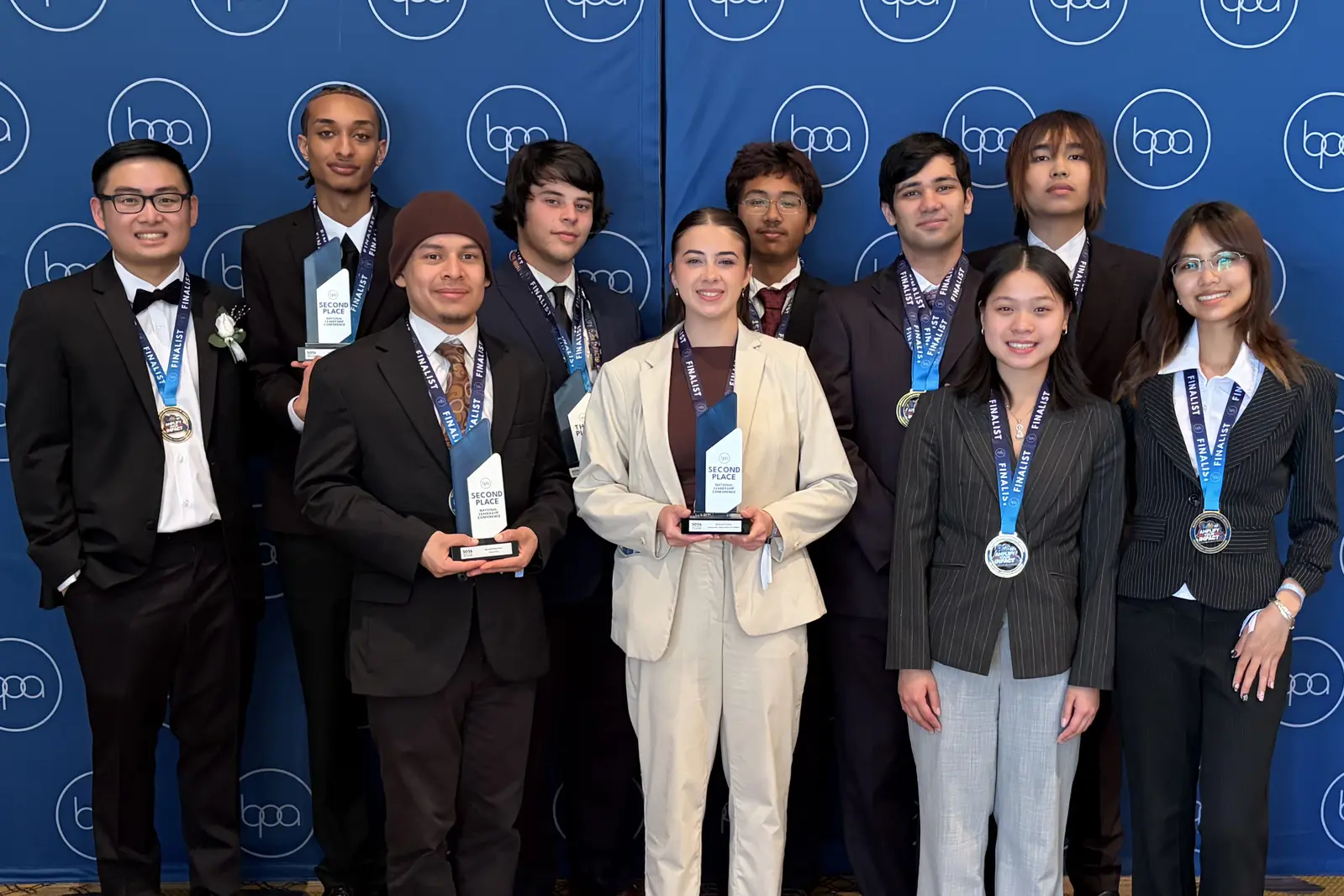 Ten young men and women in professional attire pose for a group photo while holding trophies and wearing medals.