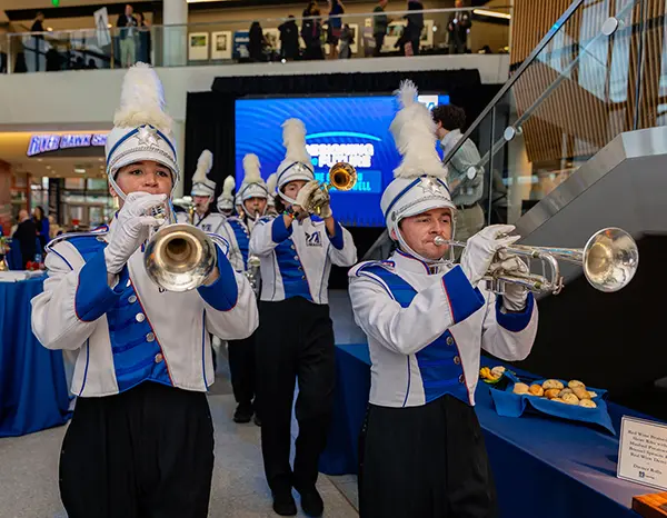 Photo shows members of the UMass Lowell Marching Band marching into University Crossing