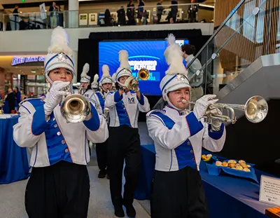 Photo shows members of the UMass Lowell Marching Band marching into University Crossing