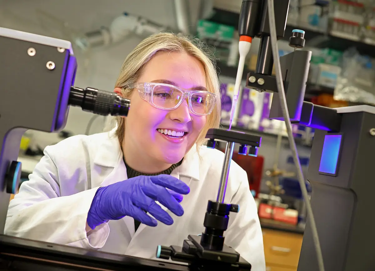 Student in a white lab coat working in lab.