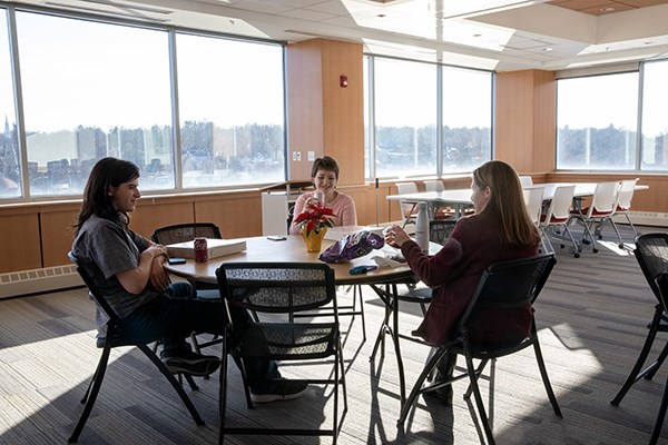 Three people sit around a table and eat lunch in a conference room with lots of natural daylight 