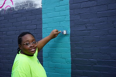 UML art major Urdilinya Smith helps paint a mural on South Campus